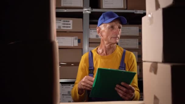 倉庫のマネージャーの古い労働者は大きな倉庫でクリップボードに書いています コピースペース — ストック動画