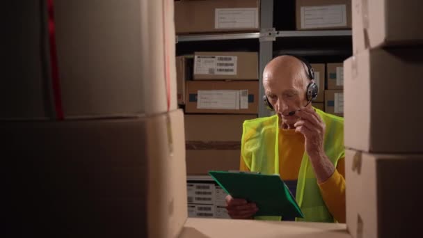 Oudere Mannelijke Professionele Operator Met Een Headset Naast Plank Percelen — Stockvideo