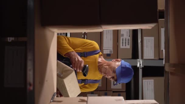 高齢の倉庫労働者は大きな倉庫の箱のバーコードをスキャンします バーティカルビデオ — ストック動画