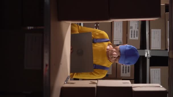 高级男性库存管理员检查库存 在笔记本电脑上打字 老人在一个堆满包裹的架子的仓库里工作 垂直录像 — 图库视频影像