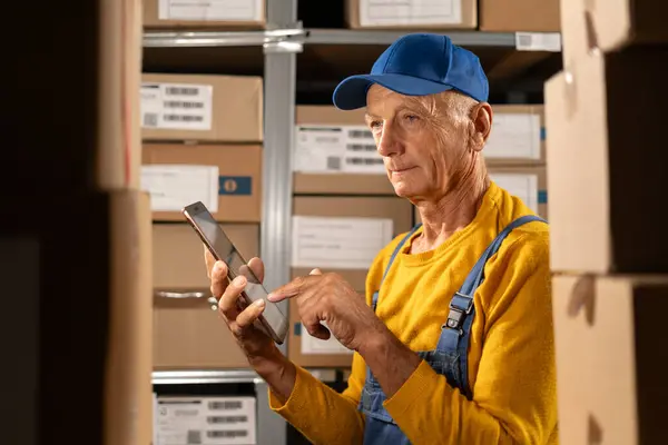 老工人用平板电脑检查库存的肖像 老人在一个堆满包裹的货架的仓库里工作 复制空间 — 图库照片