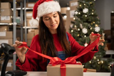 Depodaki masada kırmızı kurdeleli hediye paketi ve teslimat paketi hazırlayan bir kadın. Noel sevkiyat konsepti