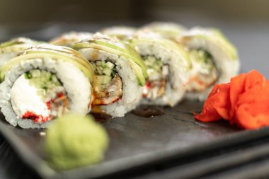 Japon yemeği. Siyah tabakta avokado ile suşi rulosu. Geleneksel suşi. Yakın plan.