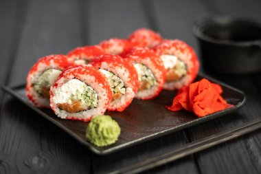 Yengeç, salatalık ve tobiko havyarlı Kaliforniya suşi rulosu. Siyah bir tabakta servis ediliyor. Tahta masada wasabi ve zencefil var. Siyah arka planda izolasyon. Japon gıda konsepti