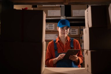 Envanteri tablet bilgisayarla kontrol eden bir kadın işçinin portresi raflarla dolu bir depoda çalışıyor. Boşluğu kopyala