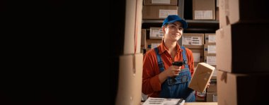 Depo teknolojileri konsepti. Malların deposu. Depoculuk işi. Tulumlu kadın kutuda barkod okuyor. Uzayı kopyala Pankart