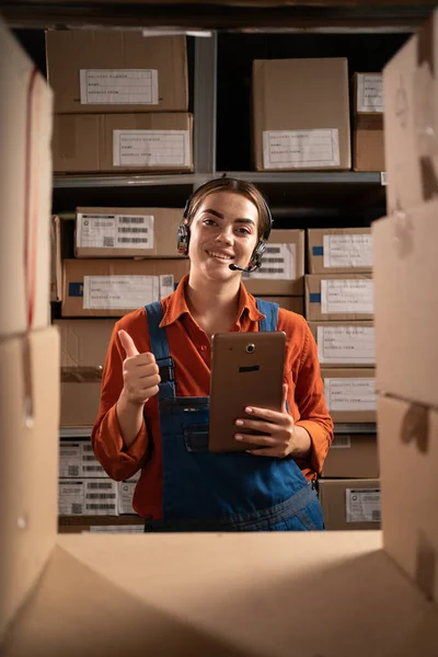 Warehouse inventory manager using digital tablet showing thumbs up gesture while looking at camera. Copy space