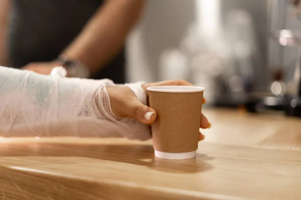 Close-up of a woman with a broken arm in a cast taking coffee to go in a cafe. Copy space