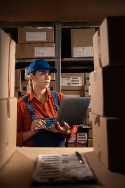 Kadın envanter müdürü depoda çalışan dizüstü bilgisayarla stokları kontrol ediyor. Boşluğu kopyala