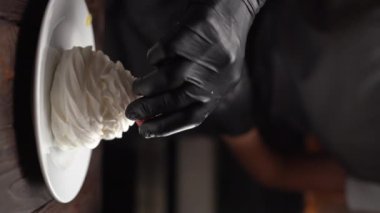 Çilekli kremalar, beyaz bir tabakta, arka planda, siyah bir masada. Şekerlemeciler elle süslenmiş böğürtlenlerle. Dikey video