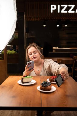 Mobil fotoğrafçı, akıllı telefon ve profesyonel fotoğrafçı teçhizatı kullanarak kafede pasta fotoğrafı çekiyor.