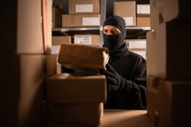 Siyah kar maskeli bir hırsız gece depoda bir paketle hırsızlık yapıyor. Depo ve mağazalardaki güvenlik sorunları kavramı. Boşluğu kopyala