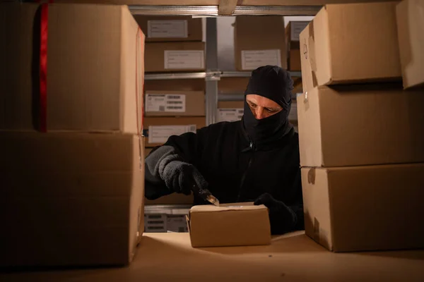 Stealing parcels and damaging the packaging of goods in the warehouse or post office. Man in balaclava and ski gloves in storehouse. Stealing and problems with the safety of cargo. Copy space