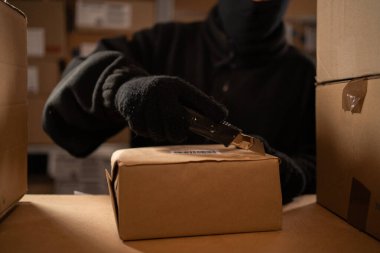 Paketleri çalmak ve ambalajdaki ya da postanedeki mallara zarar vermek. Kar maskeli bir adam ve depoda eldivenler. Çalmak ve kargo güvenliğiyle ilgili sorunlar. Yakın plan.