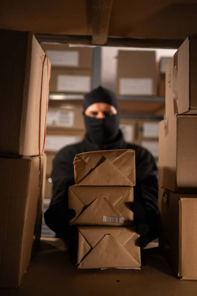 Thief wears gloves steal boxes of goods in a warehouse in the dark. Concept of problems with theft of postal parcels. Copy space