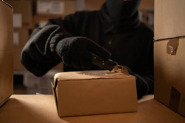 Stealing parcels and damaging the packaging of goods in the warehouse or post office. Man in balaclava and gloves in storehouse. Stealing and problems with the safety of cargo. Close-up
