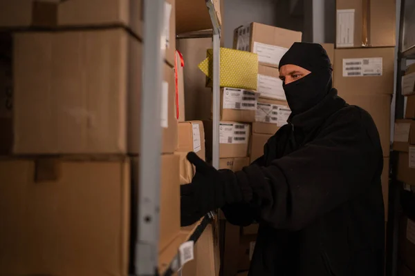 Thief in black gloves take a boxes of goods in a warehouse at night. Security problems in warehouses and stores. Copy space