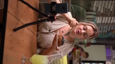 Seyahat eden kadın vlogcu, medya platformu, sosyal medya etkileyicisi, kafede yemek videosu için canlı yayın yaparken restoran yemekleri tanıtıyor. Dikey video