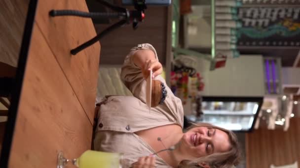 年轻女性博客为餐厅食品频道录制视频 有影响力的人在咖啡店的三脚架上安装了她的手机 垂直录像 — 图库视频影像