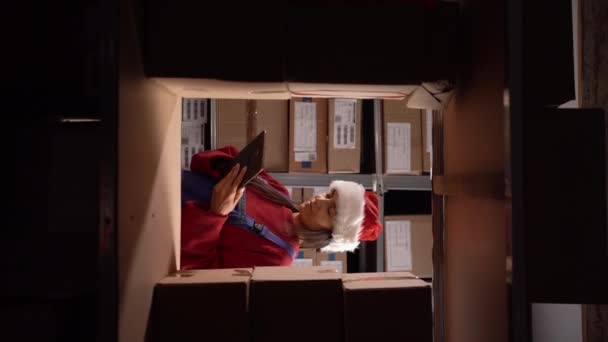 クリスマスイブでの出荷準備ができている製品と小包の在庫で働くデジタルタブレットを備えた女性の在庫管理者 バーティカルビデオ — ストック動画