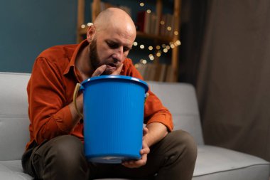 Hasta karnı olan sakallı bir adam kanepeye oturmuş kusuyor. Boşluğu kopyala