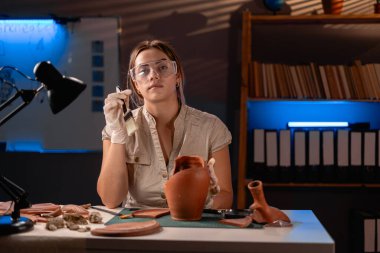 Arkeolog, eski vazo ve fırçayla geç saatlere kadar ofiste çalışıyor. Boşluğu kopyala