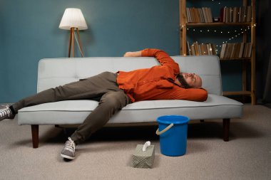 Alkol zehirlenmesi konsepti. Evde alkol içtikten sonra elinde kovayla sarhoş beyaz bir adam. İçki zehirlenmesi. Boşluğu kopyala