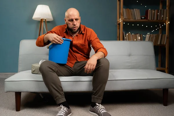 Hasta midesi ve kusmuğu olan bir adam evdeki kanepede oturuyor. Boşluğu kopyala