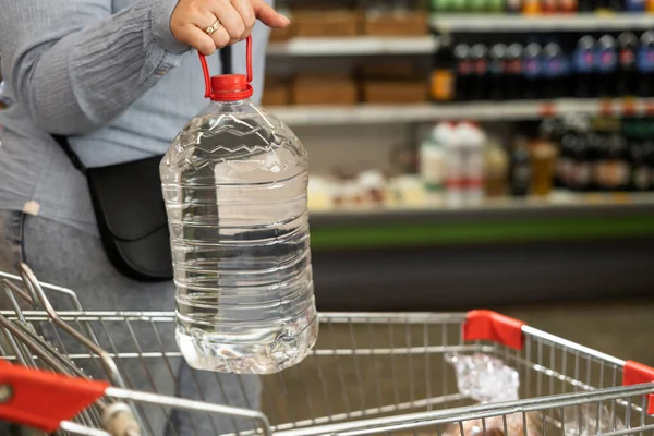 Der Käufer Hält Eine Plastikflasche Trinkwasser Der Nähe Des Einkaufswagens — Stockfoto
