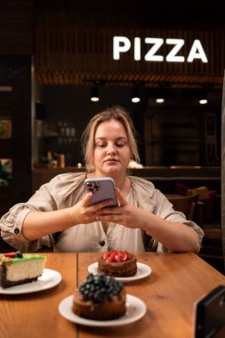 Blogcu kadınlar kafede pasta yer. Güzel bir kız sosyal medya için kek fotoğrafı çeken bir teknoloji cep telefonu kullanıyor. Boşluğu kopyala