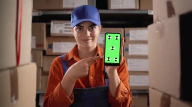 Depo çalışanı elinde cep telefonu, krom ekranda ve perakende paketlerini kontrol ediyor. Boşluğu kopyala