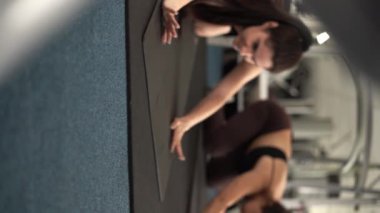 İki kız, Superman 'i siyah bir paspasın üstünde destekliyor. Isome egzersizi. Spor salonunda bel kaslarını çalıştırmak ve eğitmek. Dikey video