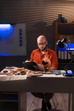 Arkeolog antika bir gemiyle çalışıyor ve gece geç saatlerde ofiste not alıyor. Boşluğu kopyala