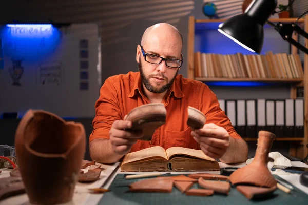 Bald archaeologist working at night in the office studying ancient artifacts. Copy space