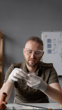 Ofiste çalışan gözlüklü bir arkeolog masada otururken antik bir tarihi eser üzerinde çalışıyor. Boşluğu kopyala