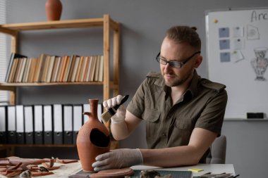 Arkeolog ofisinde çalışıyor, antik medeniyet kültürü kalıntılarını araştırıyor, fırçayla temizliyor. Boşluğu kopyala