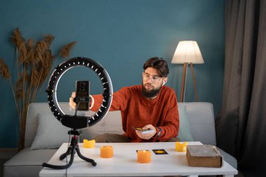 Online astroloji. Erkek falcı akıllı telefon kullanıyor, tahminler için tarot kartları okuyor, cep telefonları aracılığıyla hizmet vererek müşterilere anlatıyor. Kehanet kavramı. Boşluğu kopyala