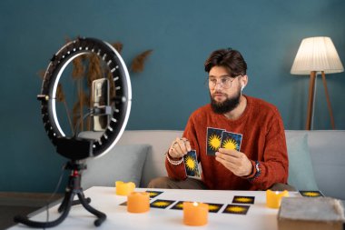 Tarot kartlı genç bir erkek falcı evdeki blog için video kaydediyor. Boşluğu kopyala