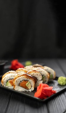 Taze çiğ somon, tütsülenmiş yılan balığı, krem peynir ve siyah ahşap arka planda avokado ile yuvarlan. kopyalama alanı. Dikey pankart