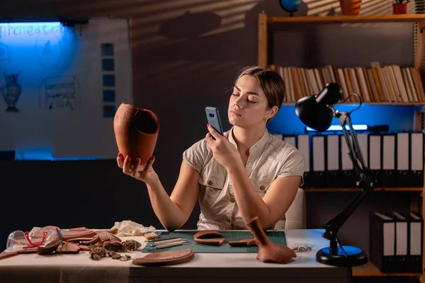 Geceleri ofiste araştırma yapan kadın arkeolog, antik medeniyet kültürü eserlerinin fotoğraflarını çekmek için akıllı telefon kullanıyor. Boşluğu kopyala