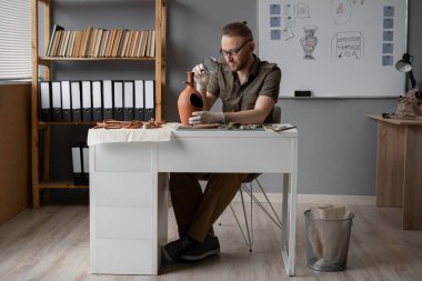 Ofiste çalışan arkeolog, antik bir amforaya büyüteçle bakıyor, antik kültürü inceliyor. Boşluğu kopyala