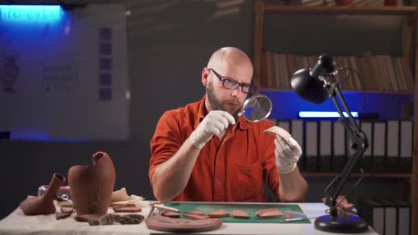 Arqueólogo Trabaja Oficina Por Noche Examinando Partes Platos Antiguos Mientras — Vídeos de Stock