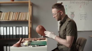 Ofiste çalışan bir arkeolog, eski bir kil eserini inceliyor. Arkeolojik çalışma. Boşluğu kopyala