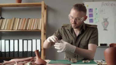 Erkek arkeolog gün boyunca ofisinde çalışırken masasında otururken antik eserler üzerinde çalışıyor. Boşluğu kopyala