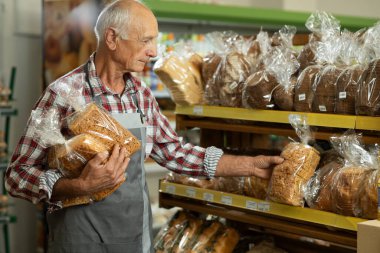 Fırınında çalışan gri önlüklü eski bir fırıncı. Süpermarkette rafa ekmek koymak. Boşluğu kopyala