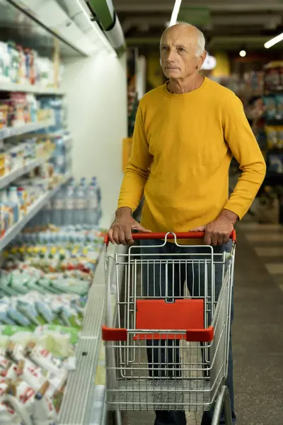 Elderly man shopping at supermarket store buy dairy produce read ingredients and prices shelf life inside hypermarket. Copy space