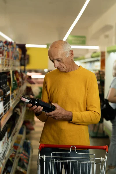 Old man chooses wine in supermarket. Elderly man reads labels on bottles of wine in supermarket. Copy space