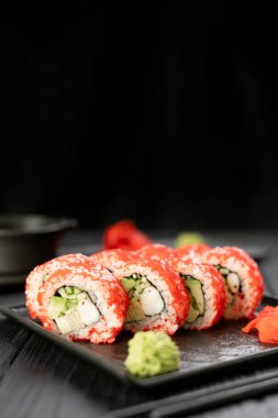 Suşi seti, havyar, avokado ve somon siyah tahta tabakta. Asya mutfağı konsepti. Boşluğu kopyala
