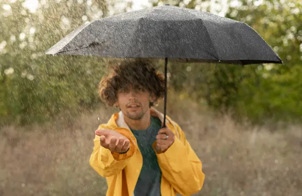 公園の雨から黒い傘カバーと黄色いレインコートの若いハンサムなアラビア人男性 コピースペース — ストック写真