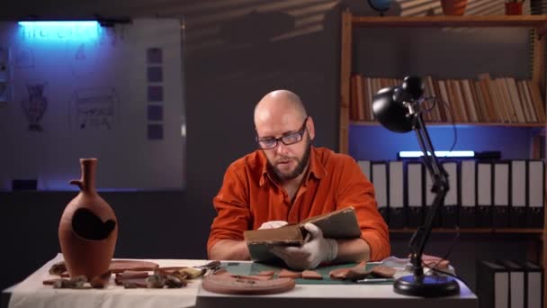 考古学家在办公室工作到深夜 阅读一本研究挖掘中发现的古董的科学书籍 复制空间 — 图库视频影像